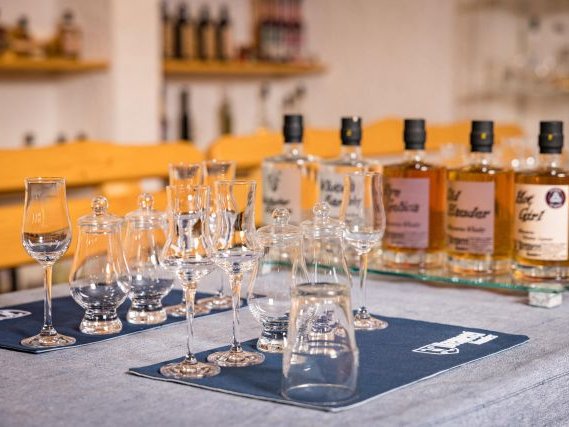 Edelbrandverkostung mit Verkostungsgläsern und verschiedenen Bränden der Brennerei Hauder im Hintergrund